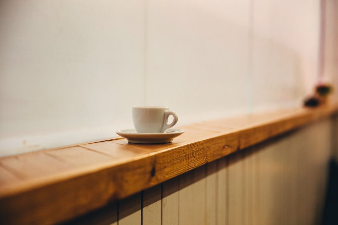 Eine Espressotasse auf der hölzernen Fensterbank vor einer hellen Wand