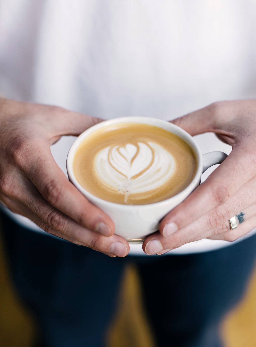 Zwei Hände halten eine Tasse Cappuccino mit Milchschaum-Herz