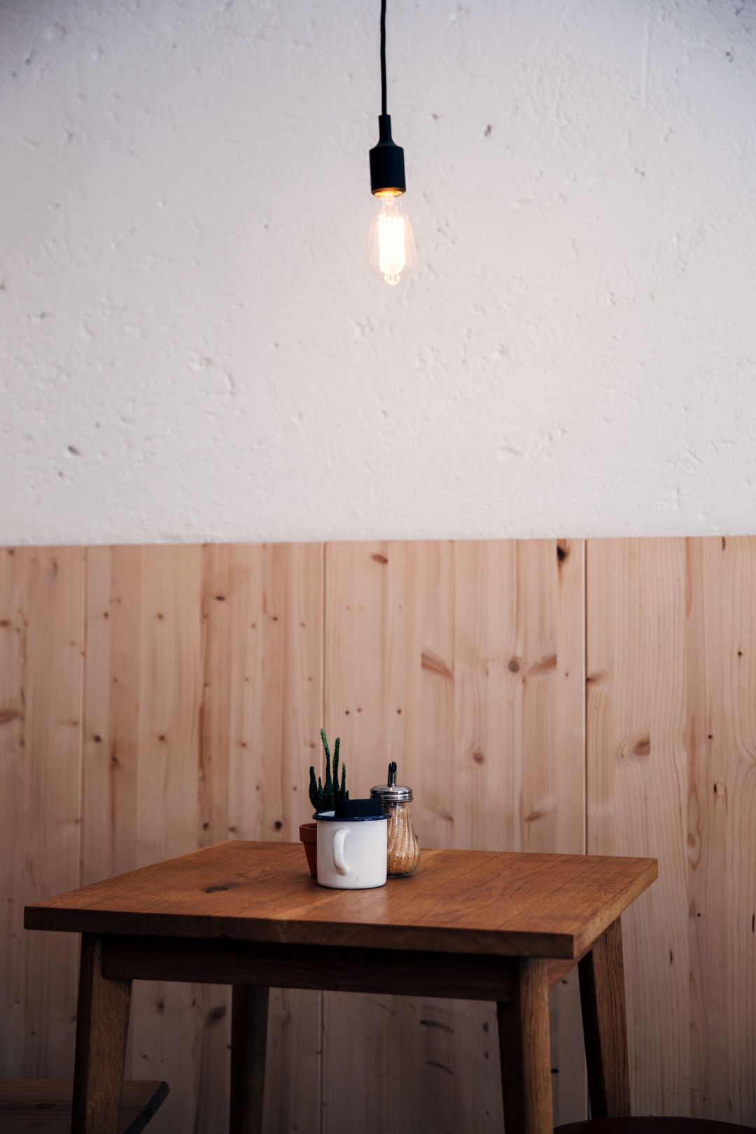 Ein kleiner Holztisch an einer holzverkleideten Wand, darüber eine Glühbirne