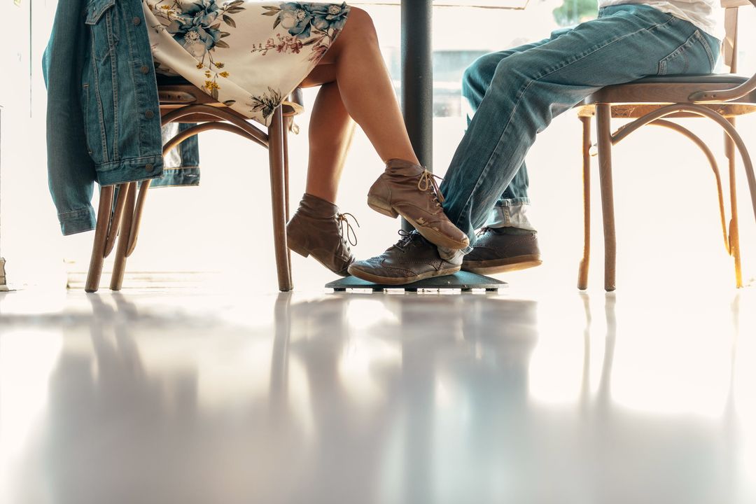 Zwei Gäste an einem Bistrotisch, man sieht nur Beine und Schuhe auf hellem Boden