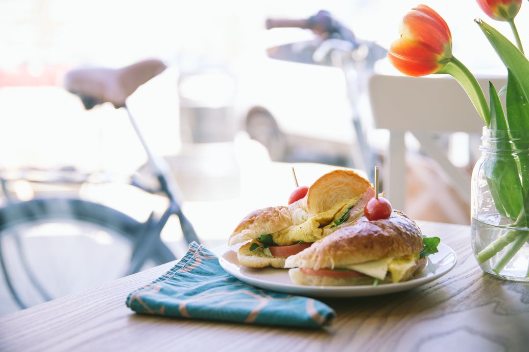 Croissant-Sandwich mit Rührei und Tomate auf einem Teller am Fenster, daneben Tulpen