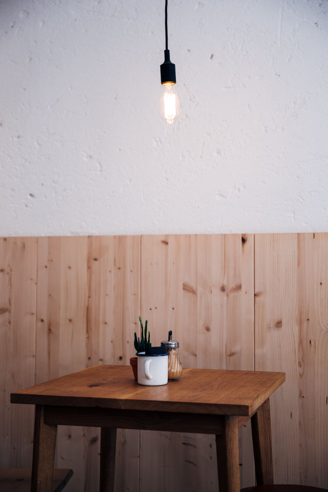 Ein kleiner Holztisch vor einer Wand mit heller Holzverkleidung, darüber eine Glühbirne
