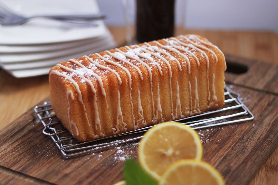 Ein glasierter Zitronenkuchen auf einem Gitter, davor Zitronenscheiben