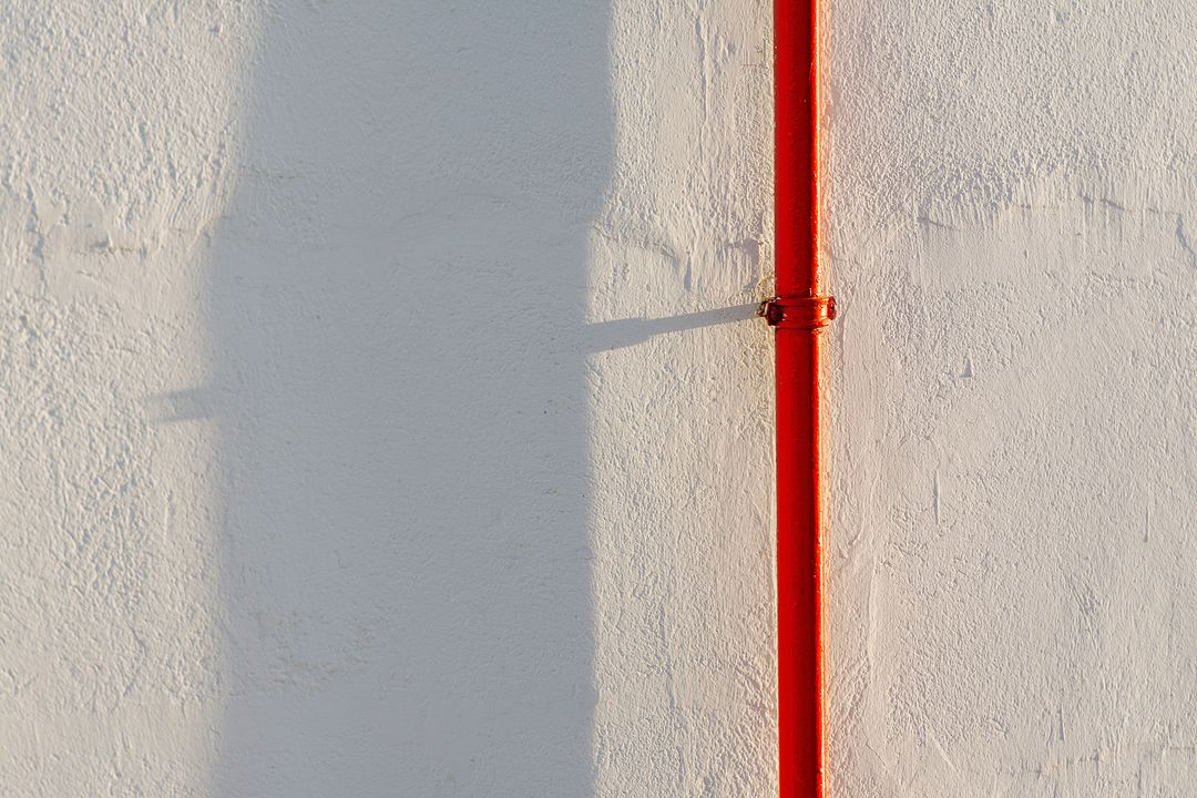 Ein rotes Heizungsrohr an einer weiß gekalkten Wand in der Sonne