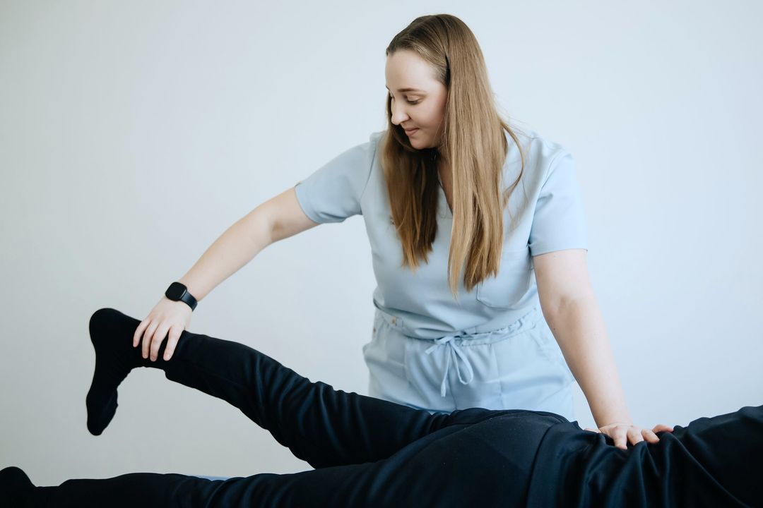 Eine Physiotherapeutin in hellblauer Praxiskleidung beugt das Bein eines liegenden Patienten