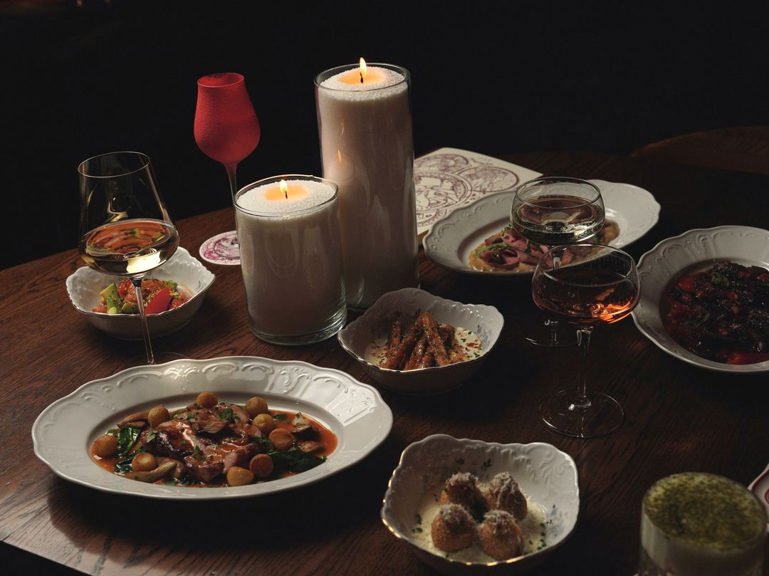 Ein Holztisch am Abend mit Kerzen, Weingläsern und vielen kleinen Tellern zum Teilen