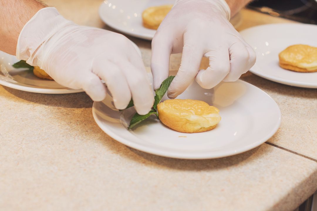 Hände in Handschuhen richten ein Dessert mit einem Minzblatt auf weißen Tellern an