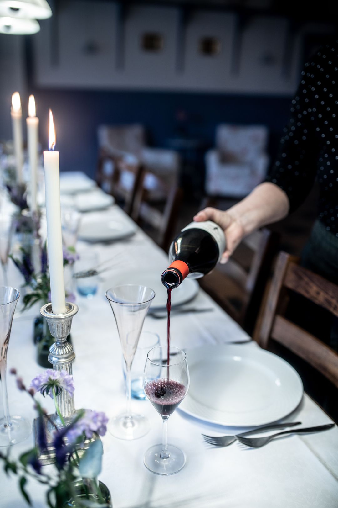 An einer langen, weiß gedeckten Tafel mit Kerzen wird Rotwein eingeschenkt