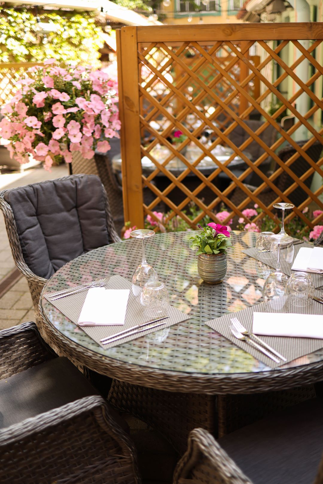 Ein gedeckter Tisch im Freien zwischen rosa Blumen und einem hölzernen Rankgitter
