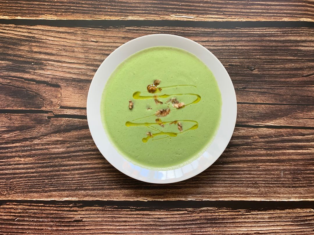 Grüne Suppe mit Öl und gerösteten Kernen in einem weißen Teller auf einem Holztisch