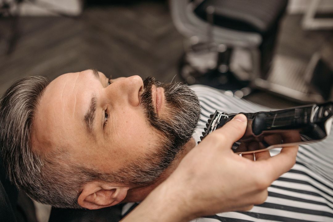 Ein Barbier trimmt einem Mann im zurückgelehnten Stuhl den Bart
