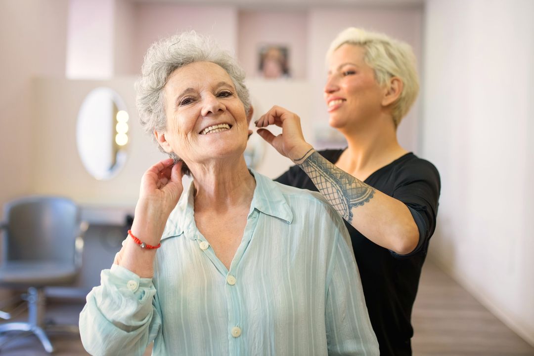 Eine Kundin lacht nach dem Schnitt, die Friseurin zupft das Haar am Ohr zurecht