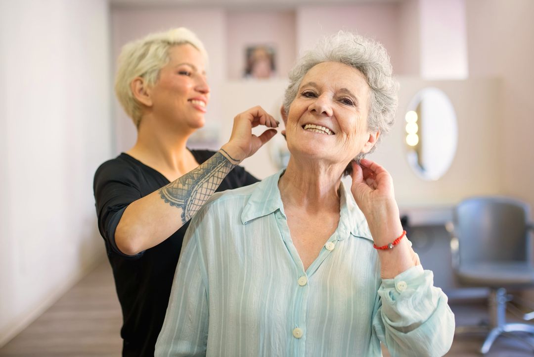 Eine Kundin lacht nach dem Schnitt, die Friseurin zupft das Haar am Ohr zurecht