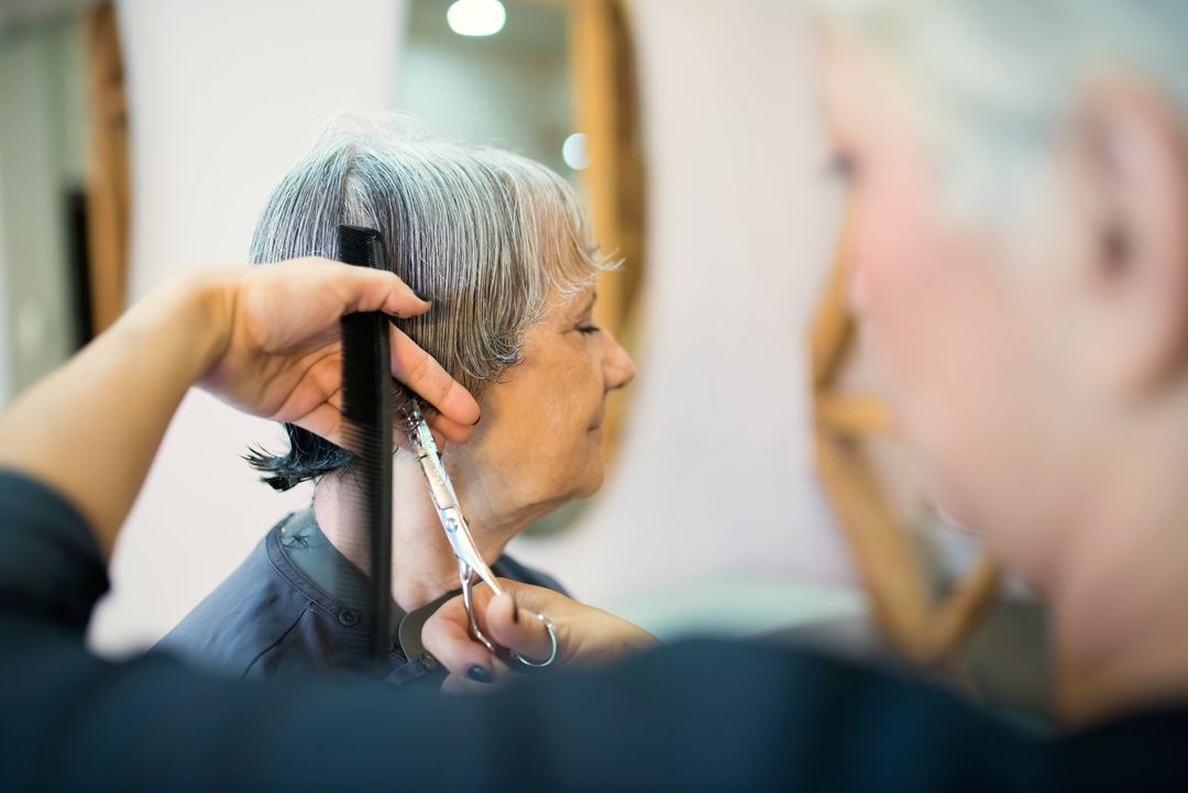 Eine Friseurin schneidet mit Kamm und Schere die Seiten eines kurzen grauen Haarschnitts