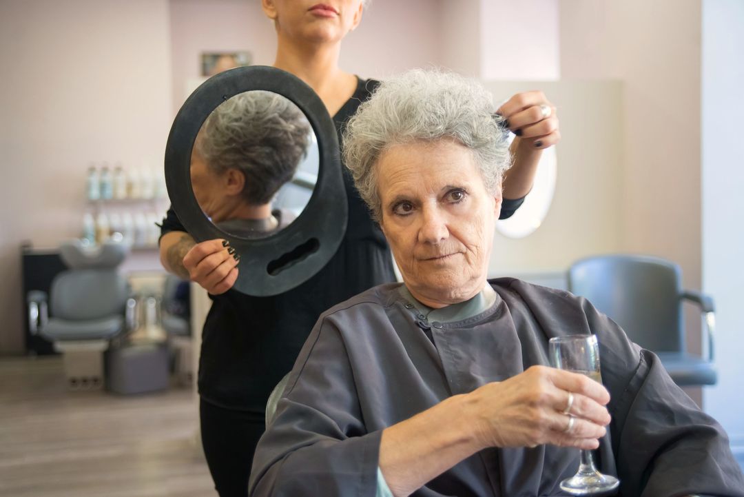 Hinter einer Kundin hält die Friseurin einen ovalen Handspiegel