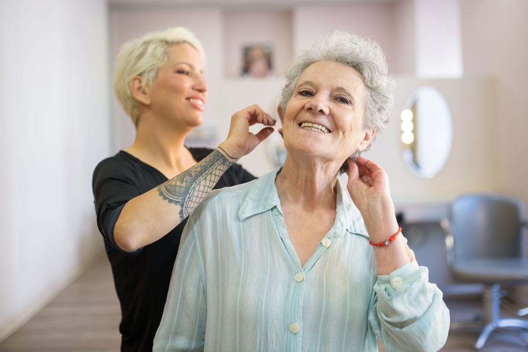 Eine Kundin mit grauem Haar lacht, hinter ihr richtet die Friseurin noch eine Strähne
