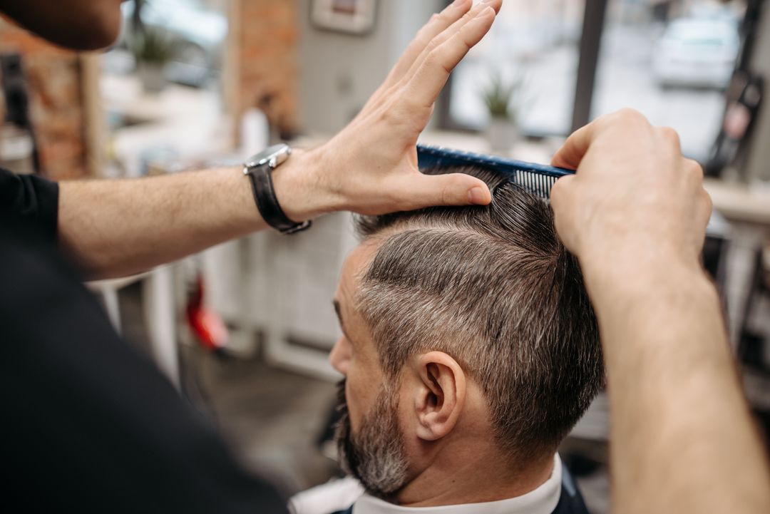 Ein Barbier zieht mit Kamm und Maschine die Seiten eines Herrenschnitts nach