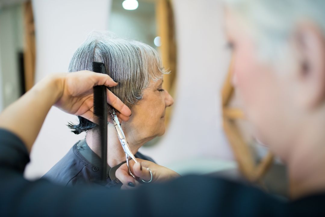 Eine Friseurin schneidet mit Kamm und Schere die Seiten eines kurzen grauen Haarschnitts