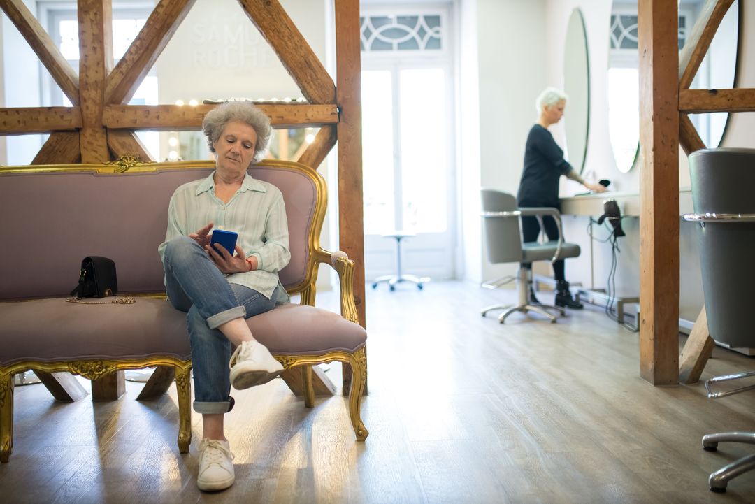 Eine Kundin wartet auf einem rosafarbenen Samtsofa mit goldenen Beinen und liest auf dem Handy