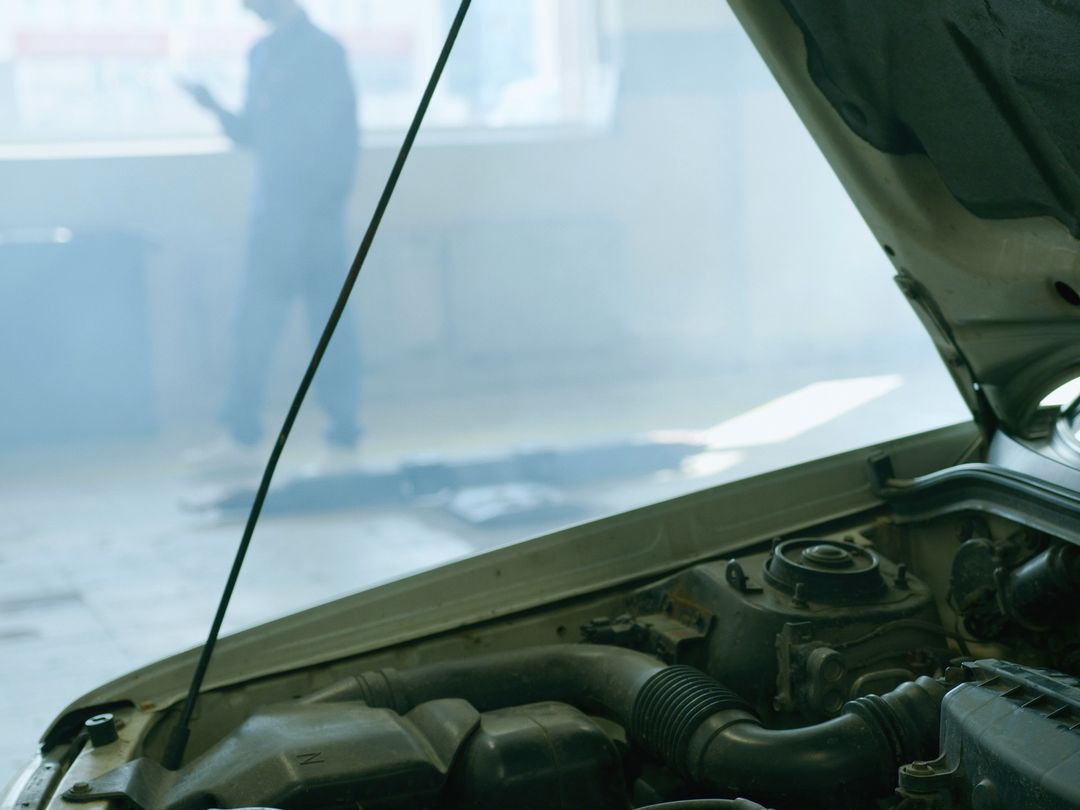 Der Motorraum eines weißen Autos unter geöffneter Haube, dahinter die Halle im Gegenlicht